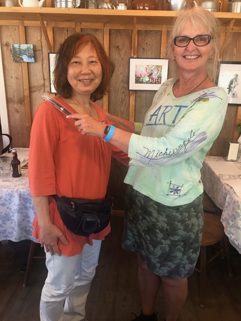 A woman in an orange shirt accepts an award from a woman in a light green shirt. 