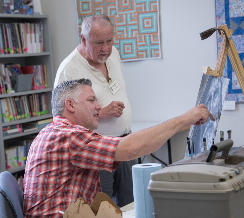 Two artists discussing art on an easel 